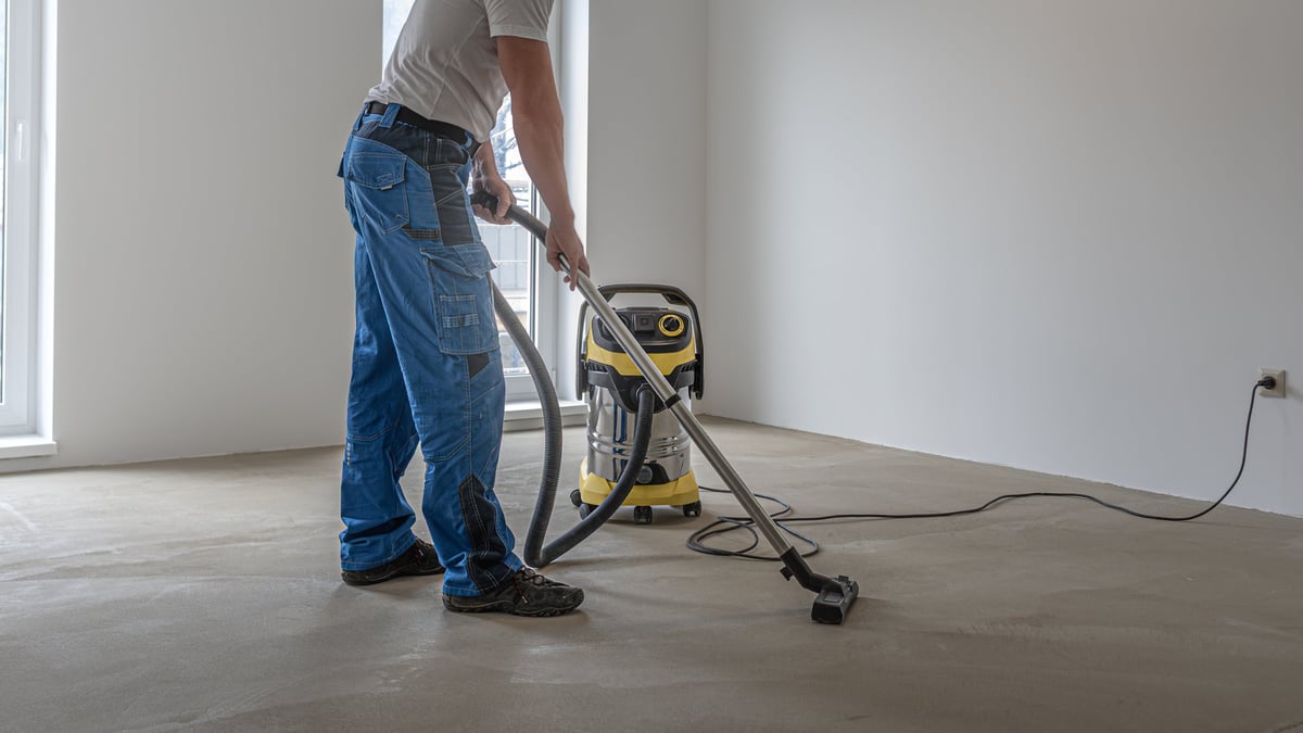 Floating floor work. A worker vacuums the floor before laying the vinyl floor layer.