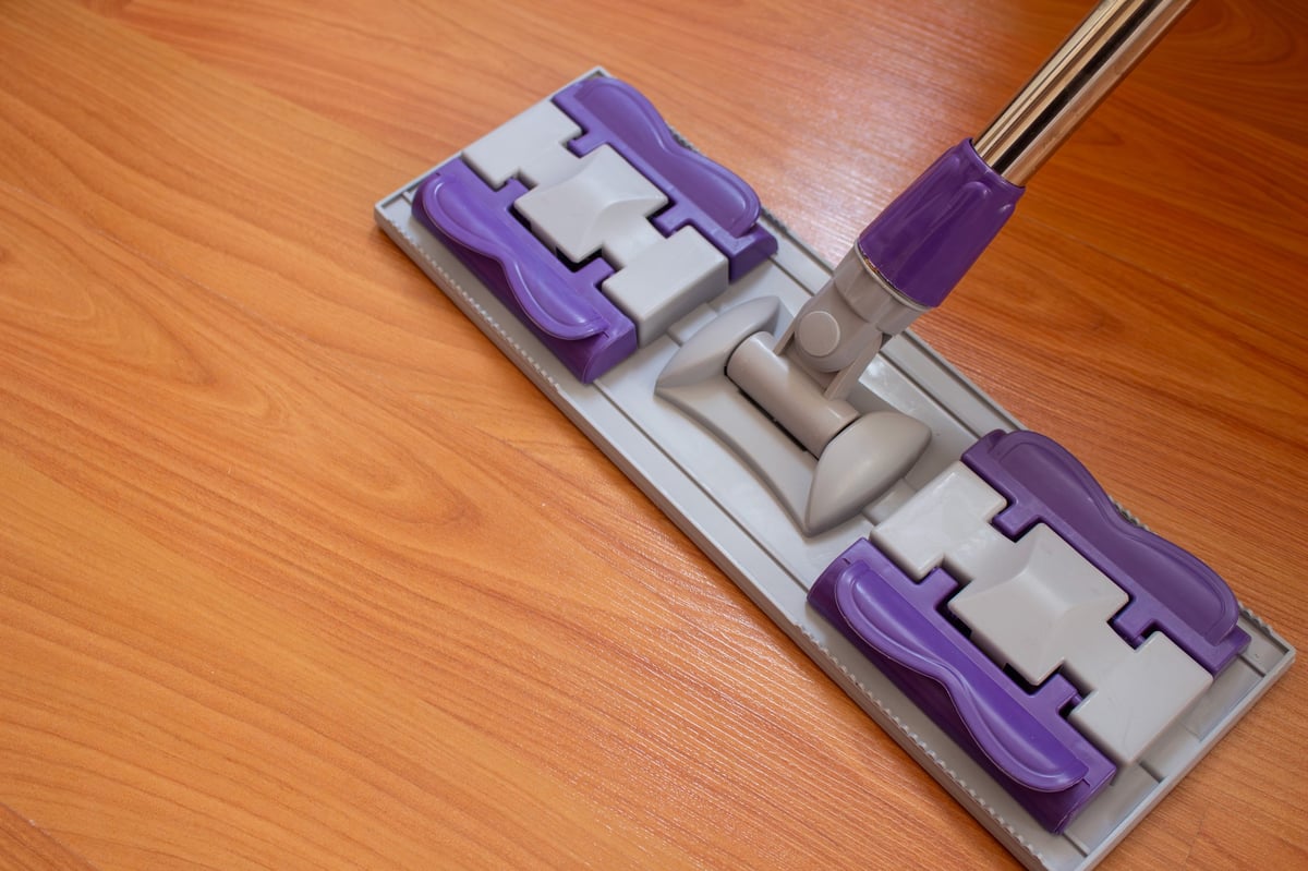 Flat mop head featuring a stylish purple and gray pattern, placed on a rich brown wooden floor, is a visual representation of household cleaning and upkeep